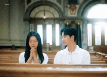 a man and a woman are sitting on a bench in a church with their hands folded in prayer .