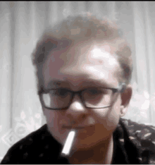 a man wearing glasses is smoking a cigarette in a close up of his face .