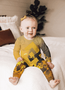 a baby is sitting on a bed wearing a yellow and brown outfit