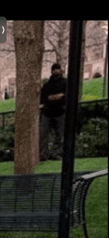 a man in a black hoodie is standing in a park behind a bench