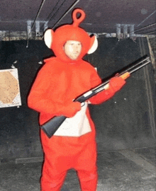 a man dressed in a red teletubbies costume holds a shotgun