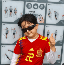 a young boy wearing sunglasses and a red adidas shirt giving a thumbs up