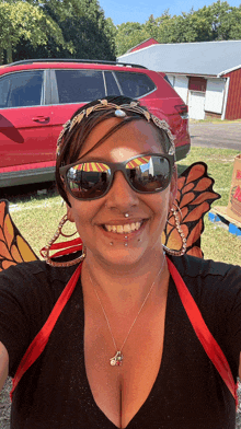 a woman wearing sunglasses and a butterfly costume is smiling in front of a red car