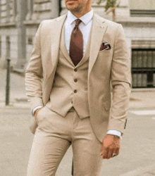 a man in a tan suit and tie is standing on the street .