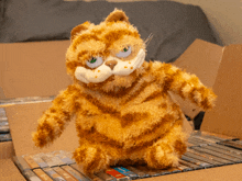 a stuffed garfield sits on top of a cardboard box filled with dvds