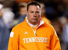 a man wearing an orange tennessee jacket looks at the camera