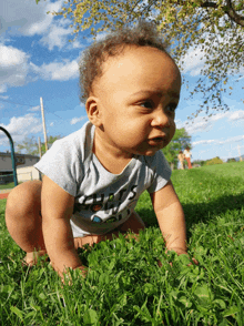 a baby crawling in the grass wearing a shirt that says ' guess ' on it