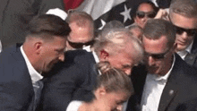 a group of people are standing around a man in a suit with a bullet in his ear .