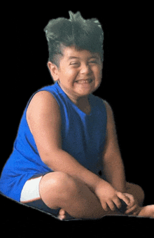 a young boy wearing a blue tank top and white shorts smiles for the camera