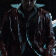 a man wearing a red leather jacket is smiling in the dark