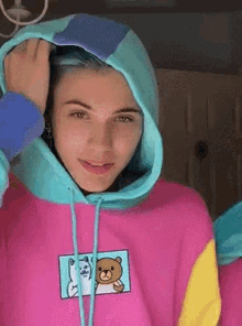 a woman with blue hair is wearing a pink and blue hoodie .