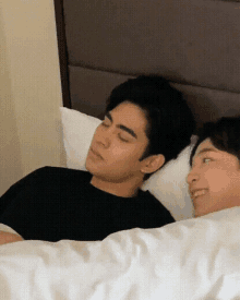 two men are laying in bed with their eyes closed and one is wearing a black shirt