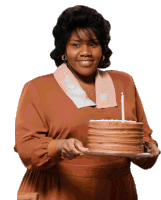 a woman in a brown dress is holding a cake with a candle in it