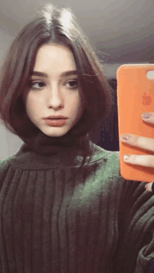 a girl in a green sweater is taking a selfie with her iphone