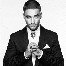 a black and white photo of a man in a suit and tie with rings on his hands .