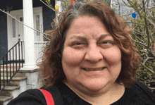 a woman with curly hair is smiling in front of a house