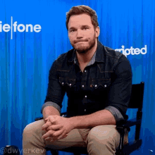 a man in a denim shirt is sitting in front of a blue curtain with the word adopted behind him