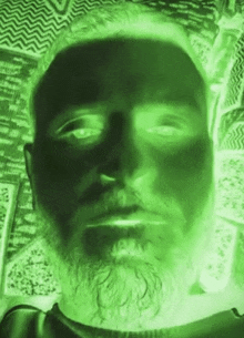 a man with a beard is taking a picture of himself with a green light behind him .