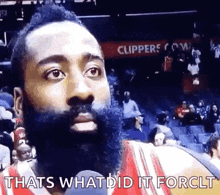 a man with a beard is sitting in the stands during a basketball game and talking into a microphone .