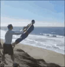 a man is holding a person in the air on the beach .