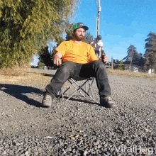 a man is sitting in a folding chair on the side of a road holding a bottle of beer .