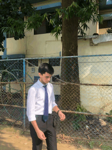 a man wearing a white shirt and blue tie is standing in front of a chain link fence