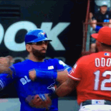 a baseball player wearing a blue jays jersey talks to another player wearing a red jersey with the number 12