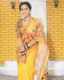 a woman wearing a yellow saree is smiling in front of a yellow brick building