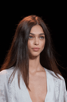 a woman with long dark hair is wearing a white top with a plunging neckline