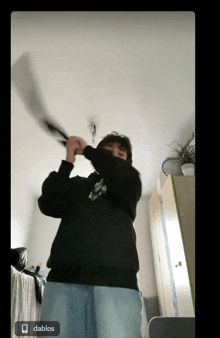 a man in a black sweatshirt is holding a bat in a room with the word dablos on the bottom