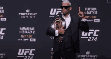 a man in a suit holds a ufc belt in front of a sign that says ufc 274