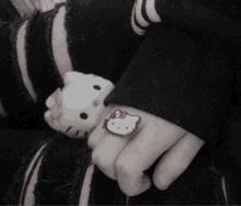 a person is holding a stuffed hello kitty and wearing a hello kitty ring .