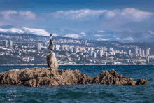 a statue of a woman standing on top of a rock overlooking the ocean