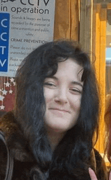 a woman with long black hair is smiling in front of a sign .