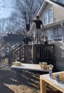 a group of people are standing on a deck in front of a house with a table full of beer cups on it