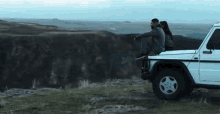 a man and a woman are sitting on the back of a white jeep on top of a hill .