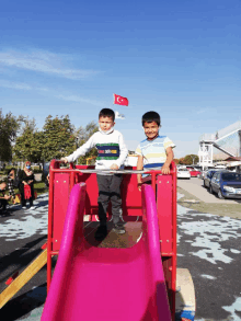 two young boys are playing on a slide with a flag in the background that says turkey