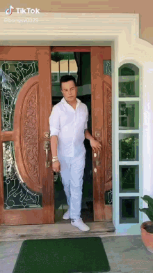 a man in a white shirt and white pants is standing in front of a door .