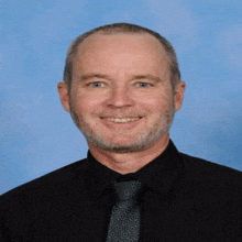 a man with a beard wearing a black shirt and tie