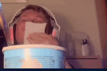 a person wearing headphones is sitting in a bowl of ice cream and covering their mouth with a piece of paper .