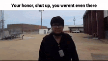 a man wearing glasses and a name tag is standing in front of a building in a dirt field .