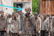 a group of zombies are walking in a line and one of them has a blue arrow pointing to him .