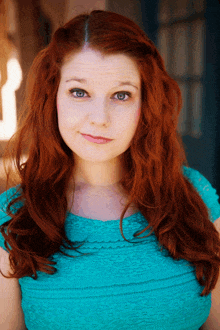 a woman with red hair and blue eyes is wearing a teal top