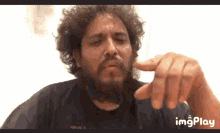 a man with curly hair and a beard is pointing at the camera with imgplay written on the bottom of the screen