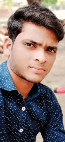 a young man is wearing a blue shirt and looking at the camera .