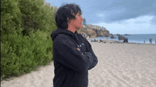 a man in a black hoodie is standing on a beach .