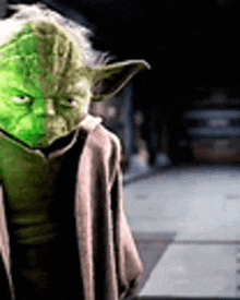 yoda from star wars is wearing a brown coat and has a green face painted on his face .