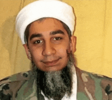 a man with a beard wearing a white turban and a camouflage jacket is smiling for the camera .