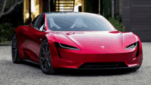 a red tesla sports car is parked in front of a house