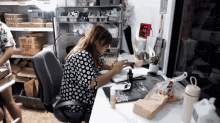 a woman in a black and white polka dot shirt sits at a desk in front of a sign that says ' chinese '